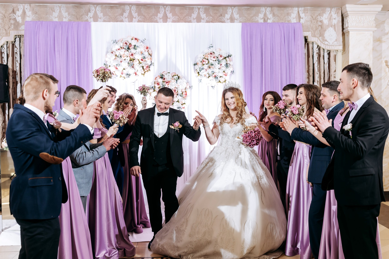 Невеста одета в длинное белое платье, а жених — в черный костюм.