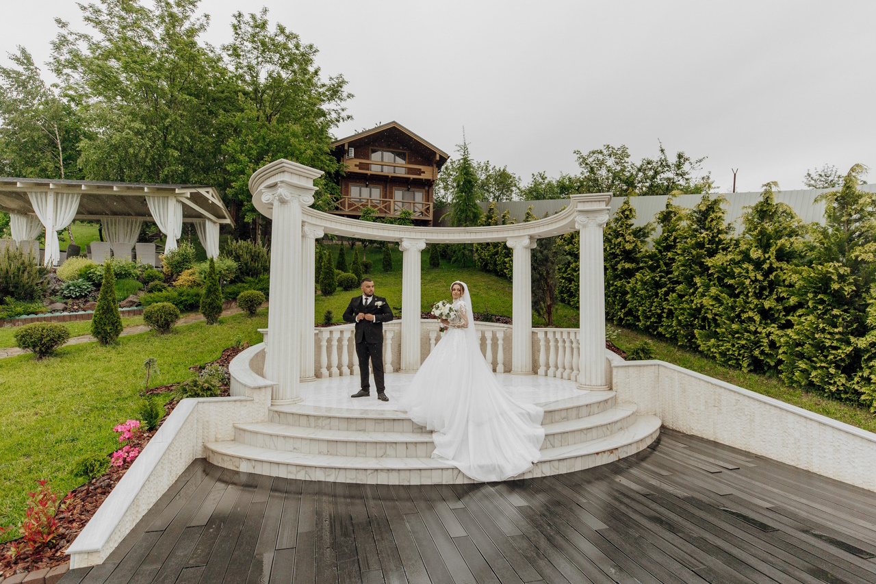 Жених и невеста стоят перед белой аркой.