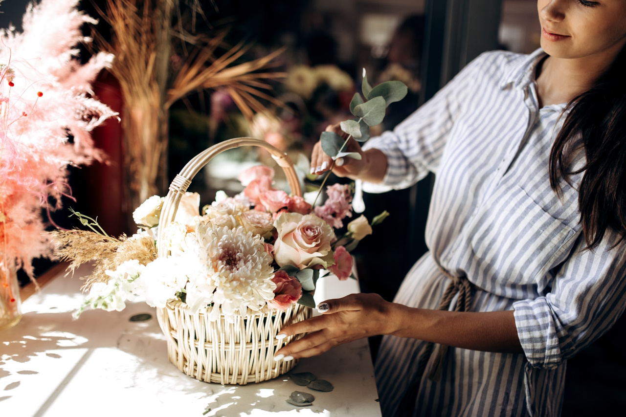 Флорист собирает букет в корзине из свежих цветов пастельных тонов в цветочном магазине